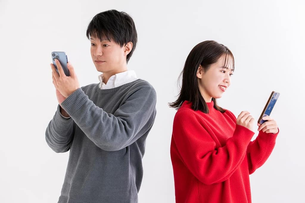 背中合わせに立ち、それぞれ自分のスマートフォンを操作している若い男女